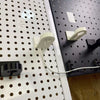 White and black Apple Watch charger holders mounted on separate round-hole pegboards.
