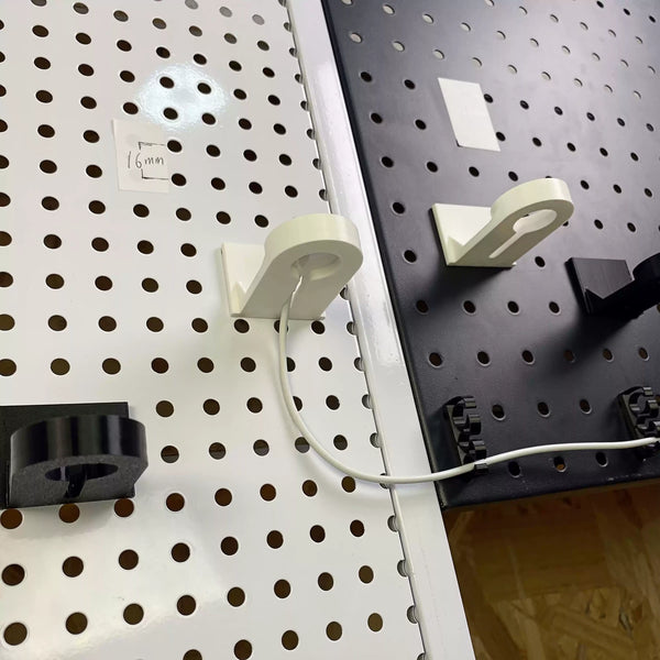White and black Apple Watch charger holders mounted on separate round-hole pegboards.
