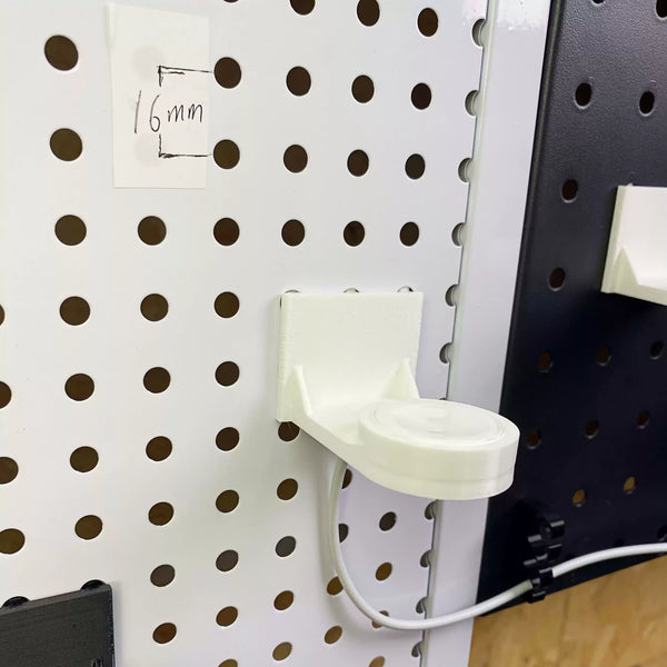 White pegboard Apple Watch charger holder mounted on a white round-hole panel.