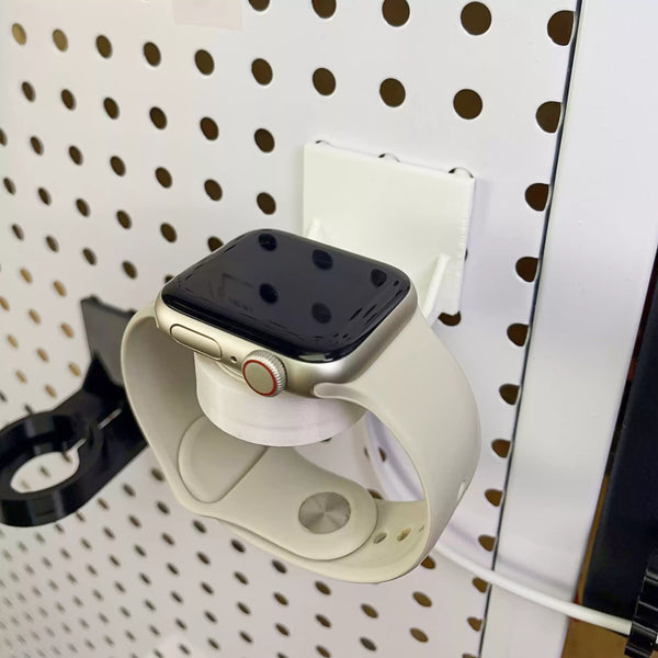 Close view of an Apple Watch on the white charger holder mounted to a round-hole pegboard.
