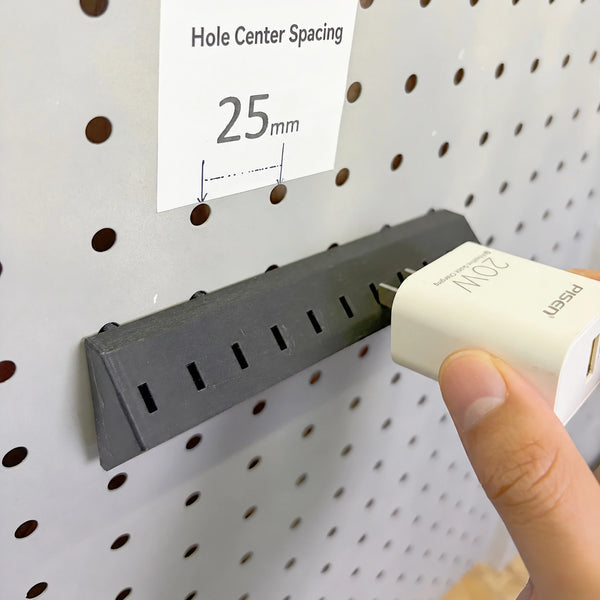 Black and white charger adapter holders mounted on a pegboard beside charging cables and a 25 mm spacing label.