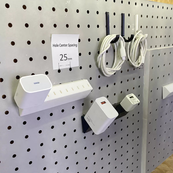 Black and white charger adapter holders mounted on a pegboard beside charging cables and a 25 mm spacing label.