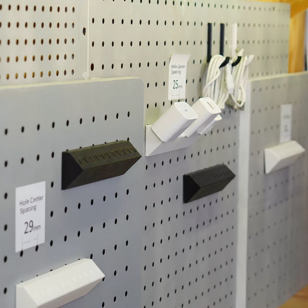 Charger adapter holders on pegboards with English hole center spacing labels of 25 mm and 29 mm.