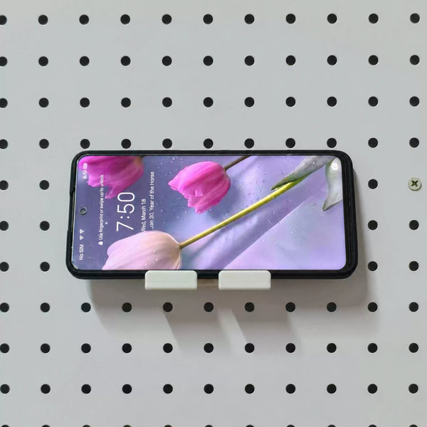 White KOKO Pegboard phone holder supporting a smartphone horizontally on a round-hole pegboard.